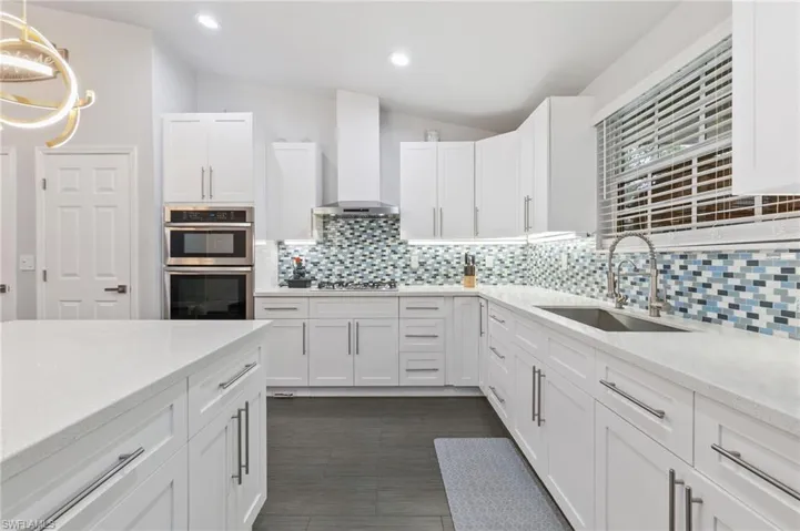 Kitchen with hanging light fixtures, sink, wall chimney range hood, and white cabinets