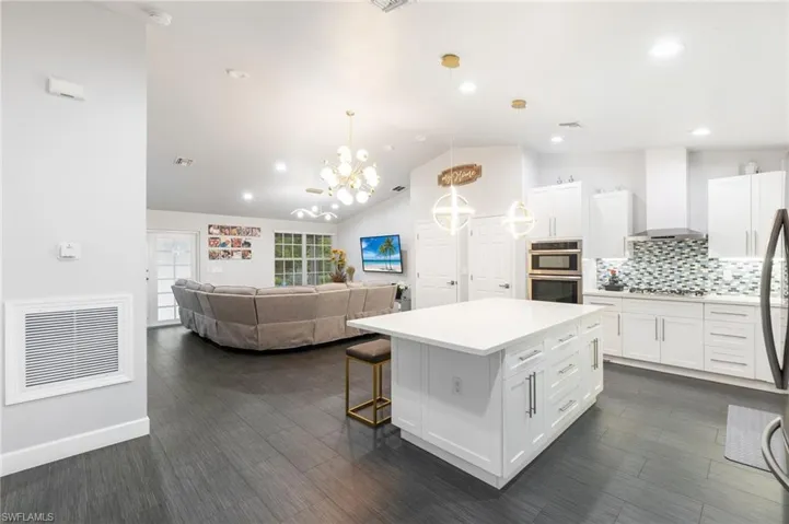 Kitchen with white cabinetry, a center island, hanging light fixtures, double oven, and wall chimney range hood