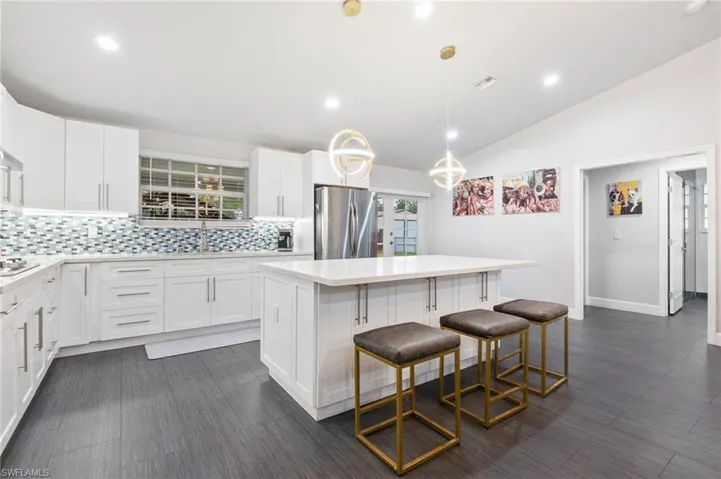 Kitchen featuring vaulted ceiling, a kitchen island, decorative light fixtures, white cabinets, and stainless steel fridge