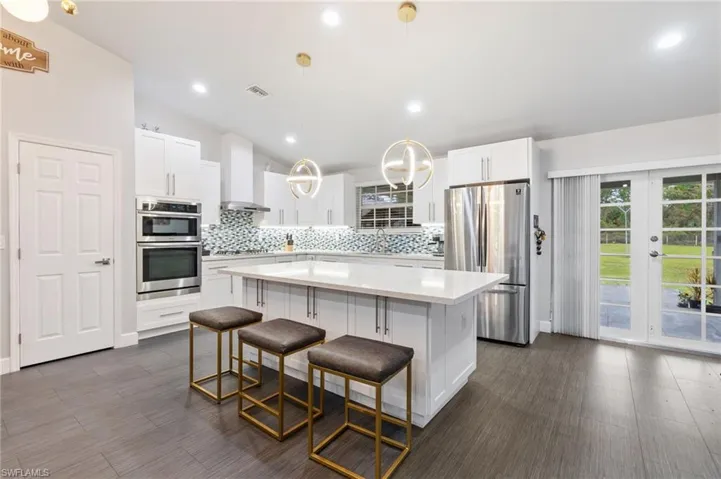 Kitchen featuring stainless steel appliances, a kitchen island, hanging light fixtures, and wall chimney exhaust hood