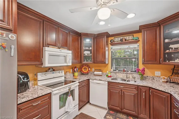 Kitchen featuring white appliances, light stone counters, light tile patterned flooring, and glass insert cabinets