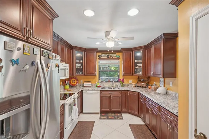 Kitchen featuring white appliances, ceiling fan, light tile patterned floors, light stone counters, and glass insert cabinets