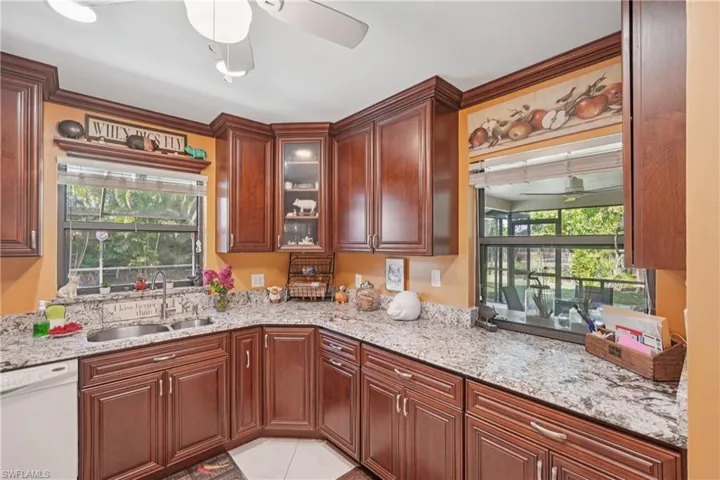 Kitchen featuring dishwasher, ceiling fan, light stone countertops, glass insert cabinets, and light tile patterned floors