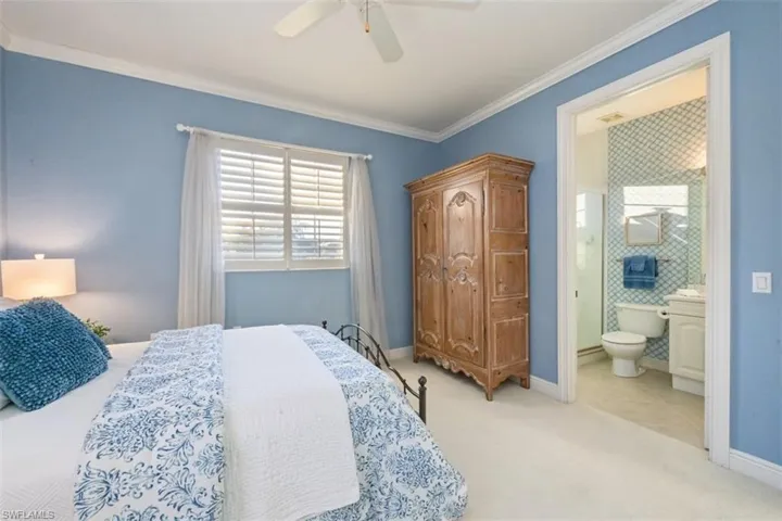 Bedroom featuring multiple windows, light carpet, ceiling fan, crown molding, and ensuite bath