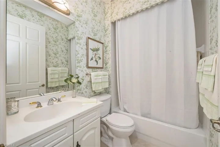Bathroom featuring vanity, shower / bath combination with curtain, wallpapered walls, and tile patterned flooring