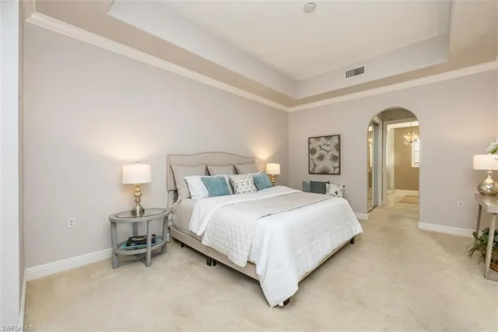 Carpeted bedroom featuring a tray ceiling, arched walkways, and ornamental molding
