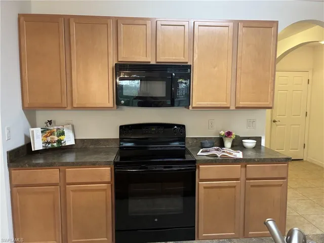 Kitchen with dark countertops, black appliances, light tile patterned floors, and arched walkways