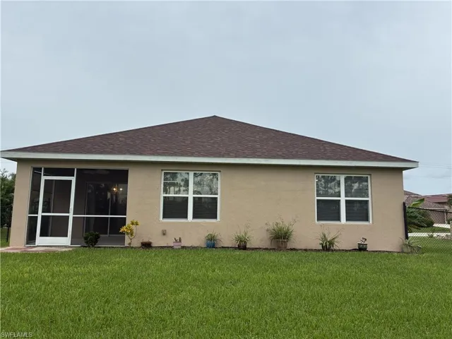 Back of property with roof with shingles, a lawn, and stucco siding
