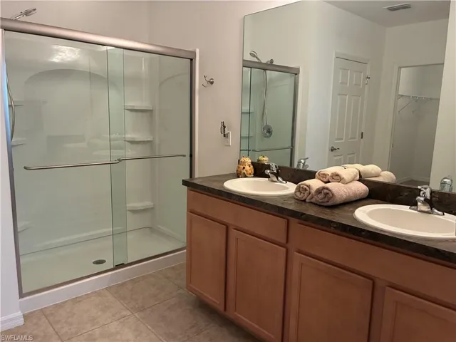 Primary Bathroom with a spacious closet, a stall shower, double vanity, and light tile patterned floors