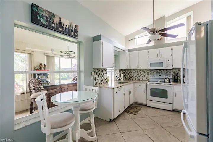 Kitchen featuring white appliances, a wealth of natural light, lofted ceiling, ceiling fan, and white cabinets