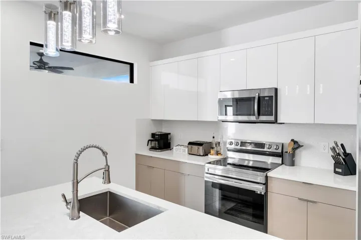 Kitchen featuring modern cabinets, stainless steel appliances, white cabinetry, light stone countertops, and pendant lighting