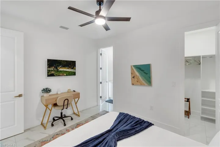 Bedroom featuring light marble finish floors, a desk, a spacious closet, and a ceiling fan