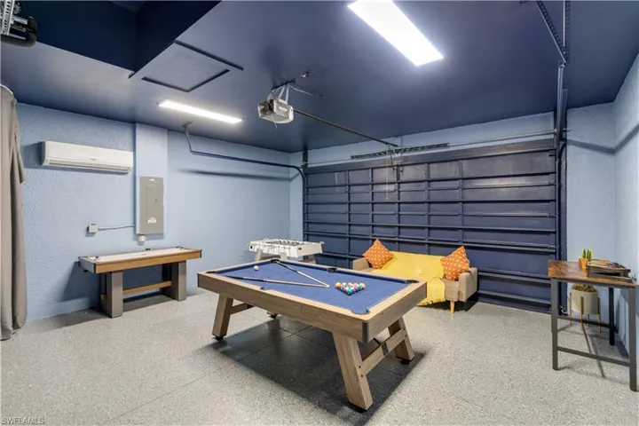 Recreation room with a textured wall, a garage, pool table, electric panel, and dark speckled floor