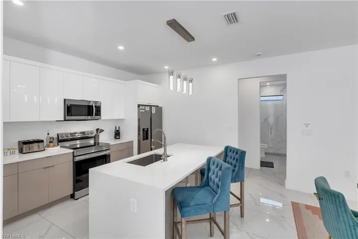 Kitchen featuring a kitchen bar, stainless steel appliances, pendant lighting, modern cabinets, and white cabinetry