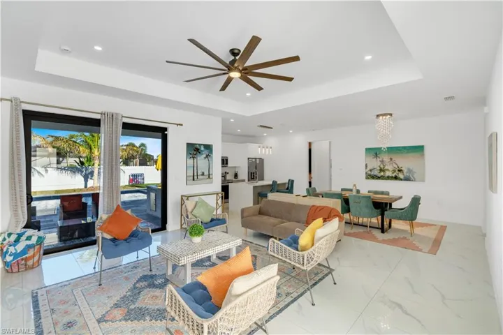 Living room with a ceiling fan, recessed lighting, a raised ceiling, a chandelier, and light marble finish floors