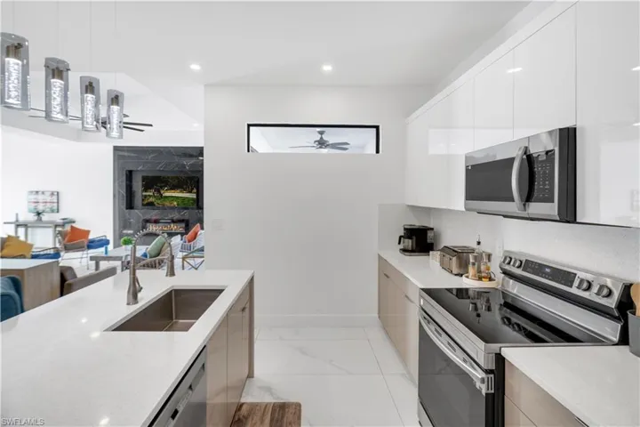 Kitchen with stainless steel appliances, modern cabinets, hanging light fixtures, light stone counters, and open floor plan