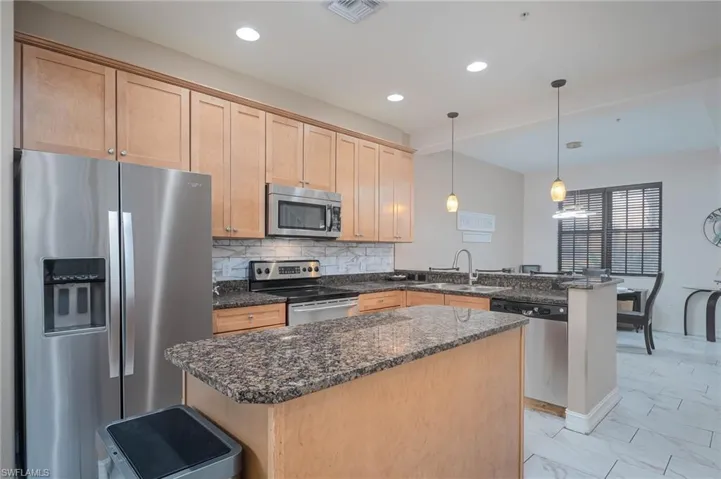 Kitchen with sink, hanging light fixtures, dark stone countertops, kitchen peninsula, and stainless steel appliances