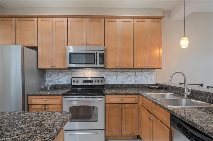 Kitchen with sink, tasteful backsplash, dark stone counters, pendant lighting, and appliances with stainless steel finishes