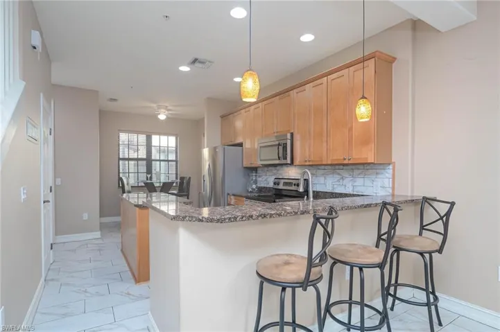 Kitchen featuring pendant lighting, dark stone countertops, appliances with stainless steel finishes, tasteful backsplash, and kitchen peninsula