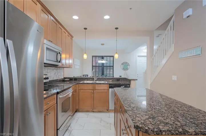 Kitchen featuring sink, hanging light fixtures, decorative backsplash, a kitchen island, and stainless steel appliances