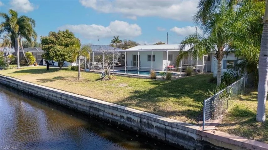 Back of property featuring a water view, an outdoor pool, a patio area, a lanai, and a fenced backyard