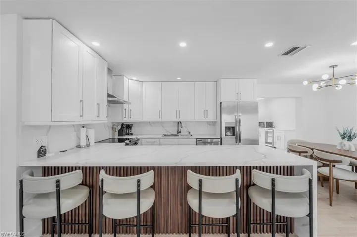 Kitchen featuring a peninsula, light stone counters, white cabinets, and stainless steel appliances