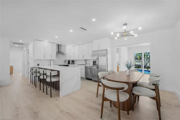 Kitchen featuring a peninsula, a kitchen bar, white cabinetry, stainless steel appliances, and light wood-style flooring