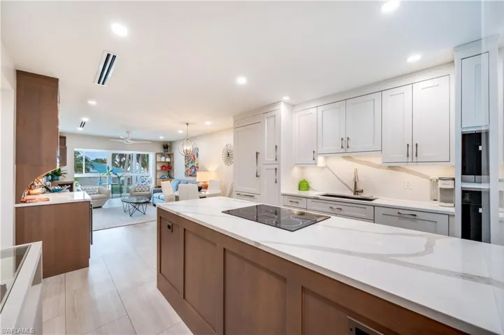 Dual tone kitchen with open floor plan, light stone counters, black electric cooktop, a ceiling fan, and hanging light fixtures