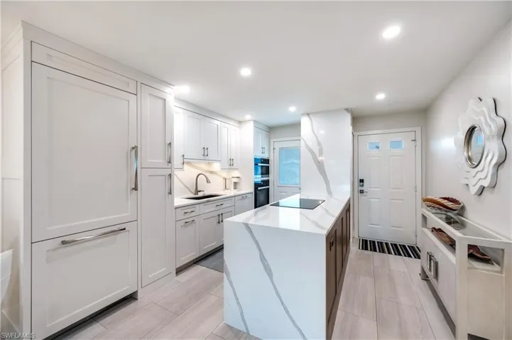 Dual tone kitchen with light stone countertops, recessed lighting, decorative backsplash, black appliances, and two tone color scheme
