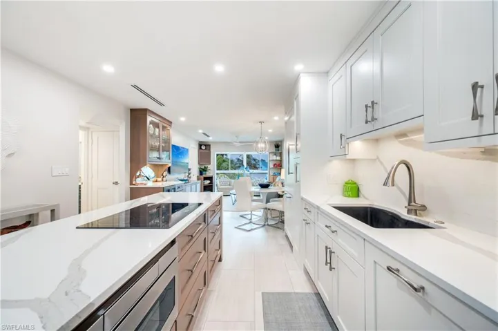 Dual tone kitchen with two tone cabinets, light stone counters, black electric stovetop, glass insert cabinets, and open floor plan