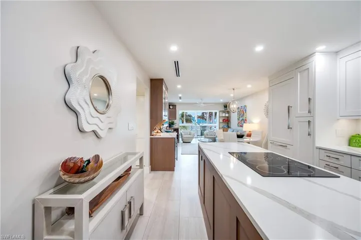 Kitchen with open floor plan, dual tone cabinets, black electric cooktop, light stone countertops, and pendant lighting