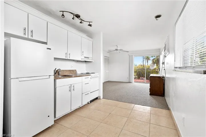 Kitchen with white appliances, white cabinetry, light colored carpet, dark countertops, and ceiling fan