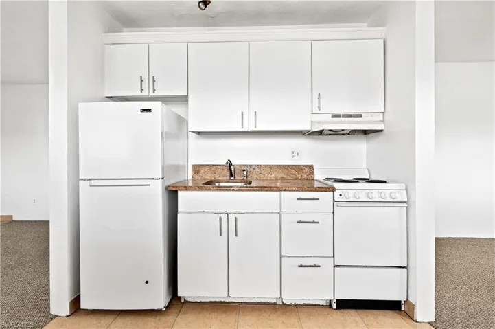 Kitchen with white appliances, white cabinetry, light carpet, and light tile patterned flooring