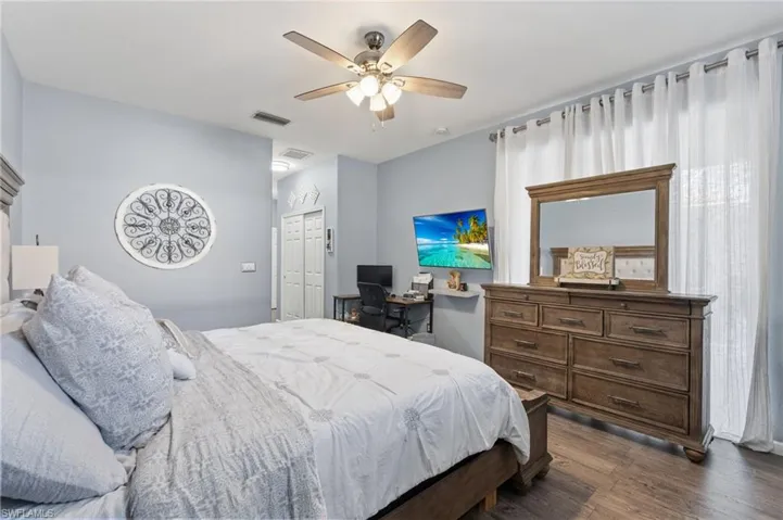 Bedroom with a closet, a ceiling fan, dark wood-type flooring, and a desk