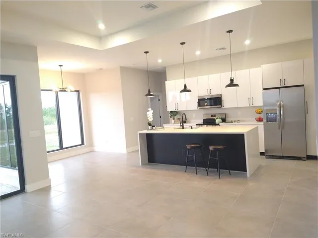 Kitchen featuring a center island with sink, pendant lighting, white cabinets, and appliances with stainless steel finishes