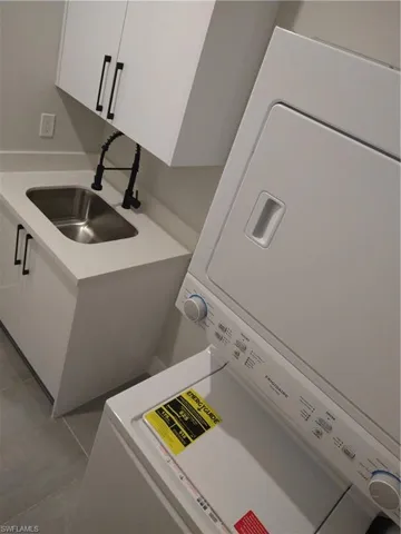 Washroom featuring cabinets, sink, light tile patterned floors, and stacked washing maching and dryer