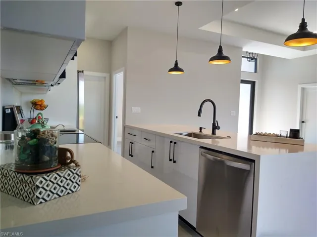 Kitchen featuring sink, stainless steel dishwasher, an island with sink, decorative light fixtures, and white cabinets