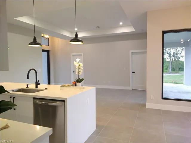 Kitchen featuring a raised ceiling, sink, pendant lighting, light tile patterned floors, and dishwasher