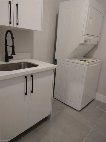 Laundry room with light tile patterned flooring, stacked washer / dryer, cabinets, and sink