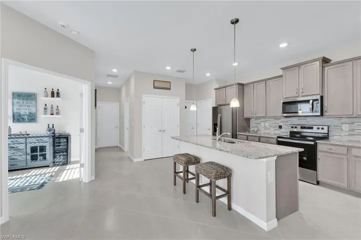 Kitchen with appliances with stainless steel finishes, light tile patterned floors, decorative backsplash, a breakfast bar, and a kitchen island with sink