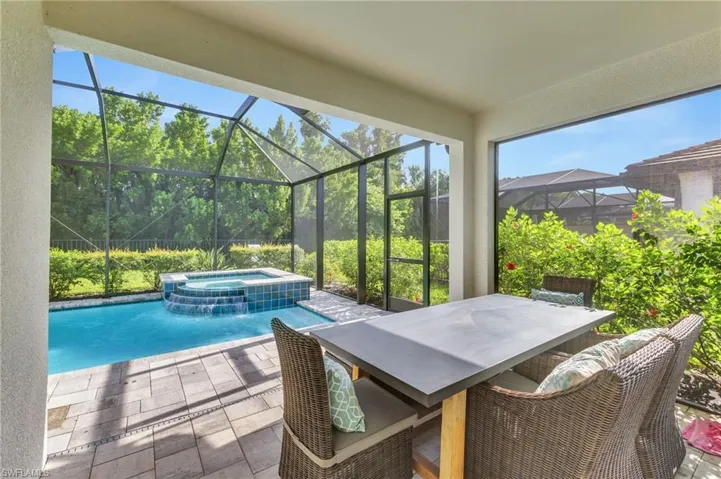 View of patio featuring glass enclosure and a pool with connected hot tub
