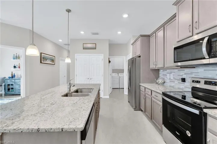 Kitchen with stainless steel appliances, washing machine and dryer, an island with sink, tasteful backsplash, and light stone countertops