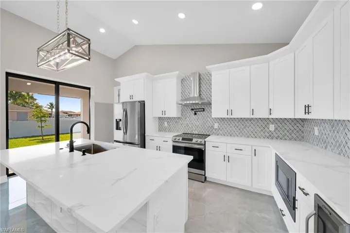 Kitchen featuring sink, stainless steel appliances, a center island with sink, and wall chimney exhaust hood