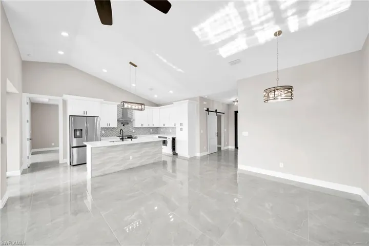 Kitchen with a barn door, decorative light fixtures, lofted ceiling, and stainless steel refrigerator with ice dispenser