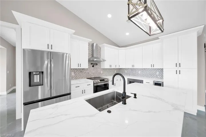 Kitchen featuring wall chimney range hood, light stone countertops, stainless steel appliances, backsplash, and pendant lighting