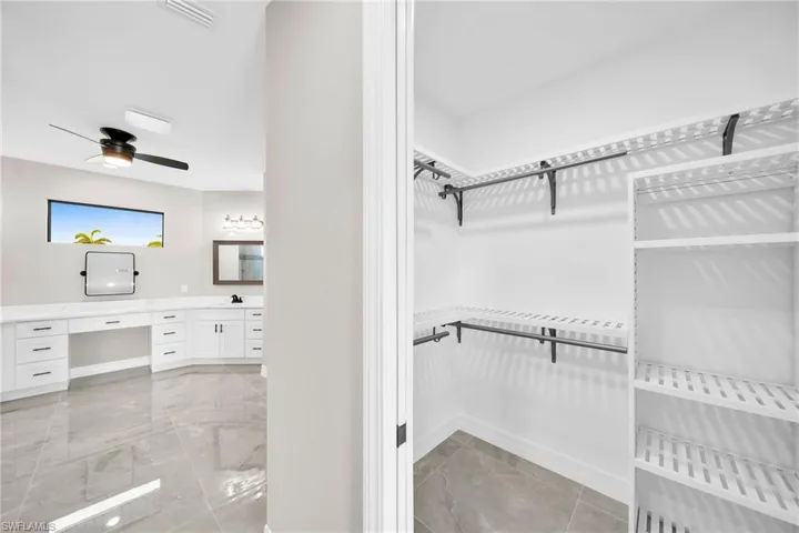 Spacious closet featuring built in desk, ceiling fan, and light tile floors