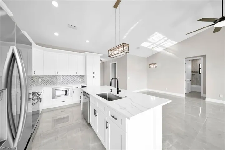 Kitchen with lofted ceiling, stainless steel appliances, sink, ceiling fan, and light tile floors