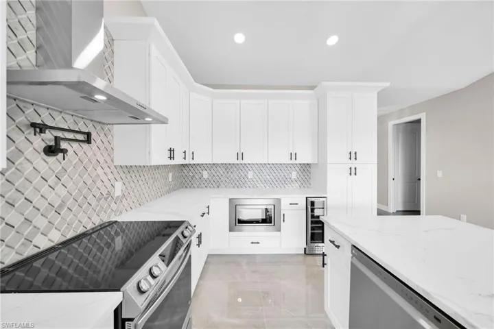 Kitchen with light stone countertops, beverage cooler, backsplash, wall chimney range hood, and appliances with stainless steel finishes