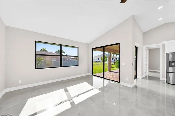 Empty room with high vaulted ceiling, ceiling fan, and light tile flooring