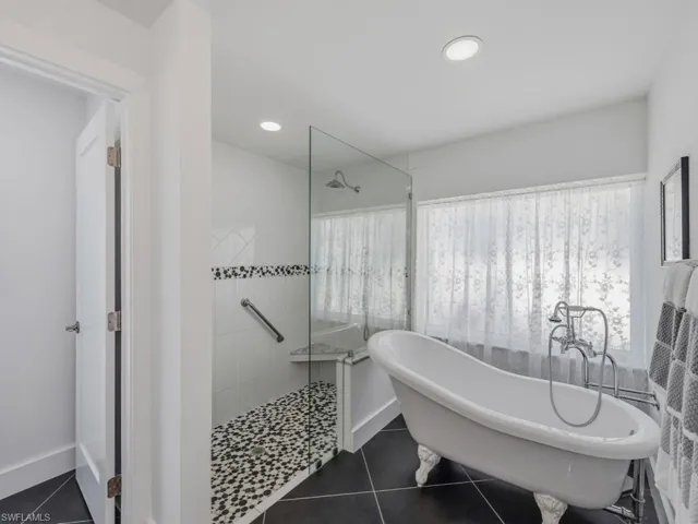 Full bathroom featuring a walk in shower, a freestanding tub, dark tile patterned floors, healthy amount of natural light, and recessed lighting